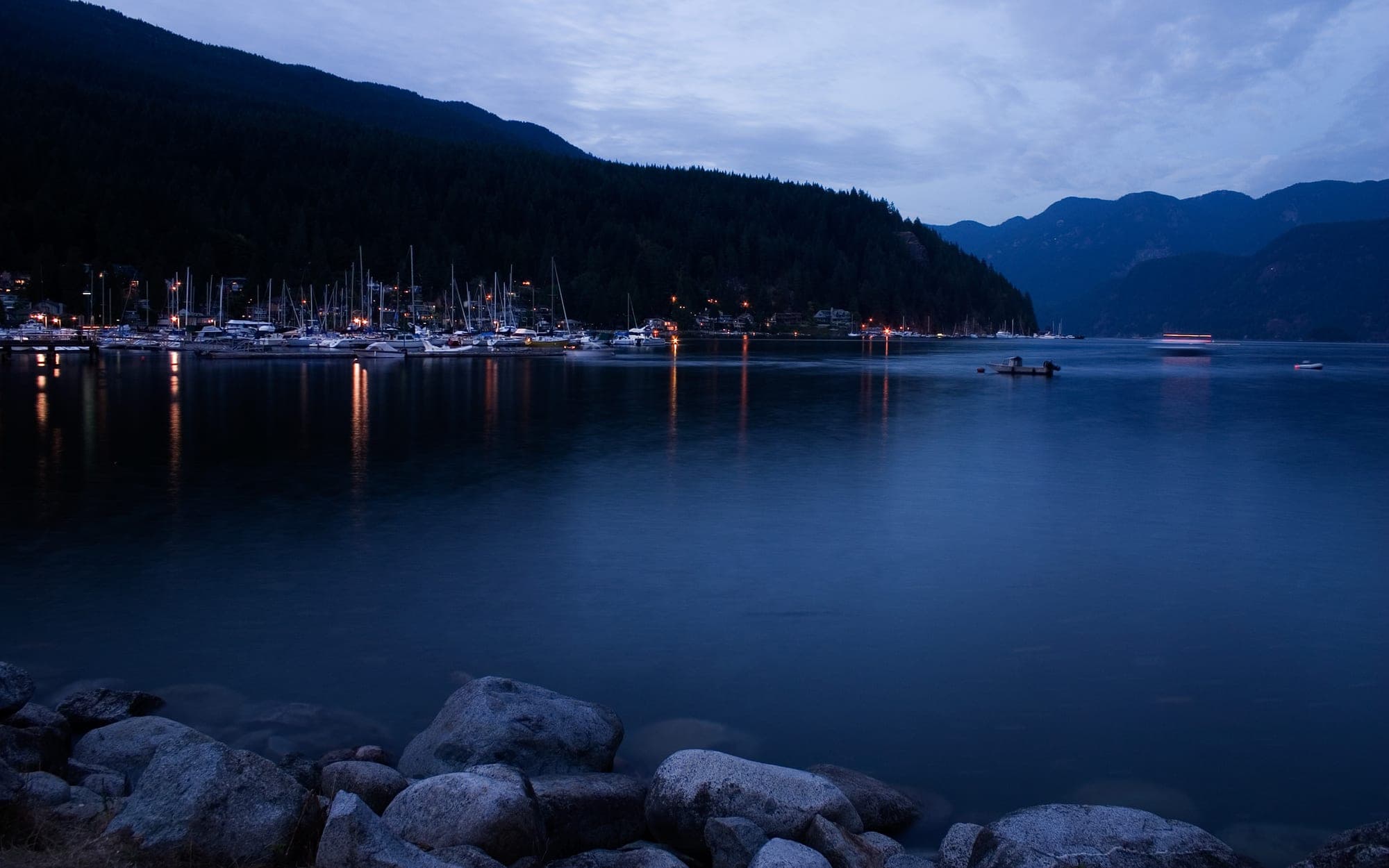 The calm waters of Deep Cove at the mouth of Indian Arm in North Vancouver, with kayaks on the beach and forested hillsides surrounding the village.