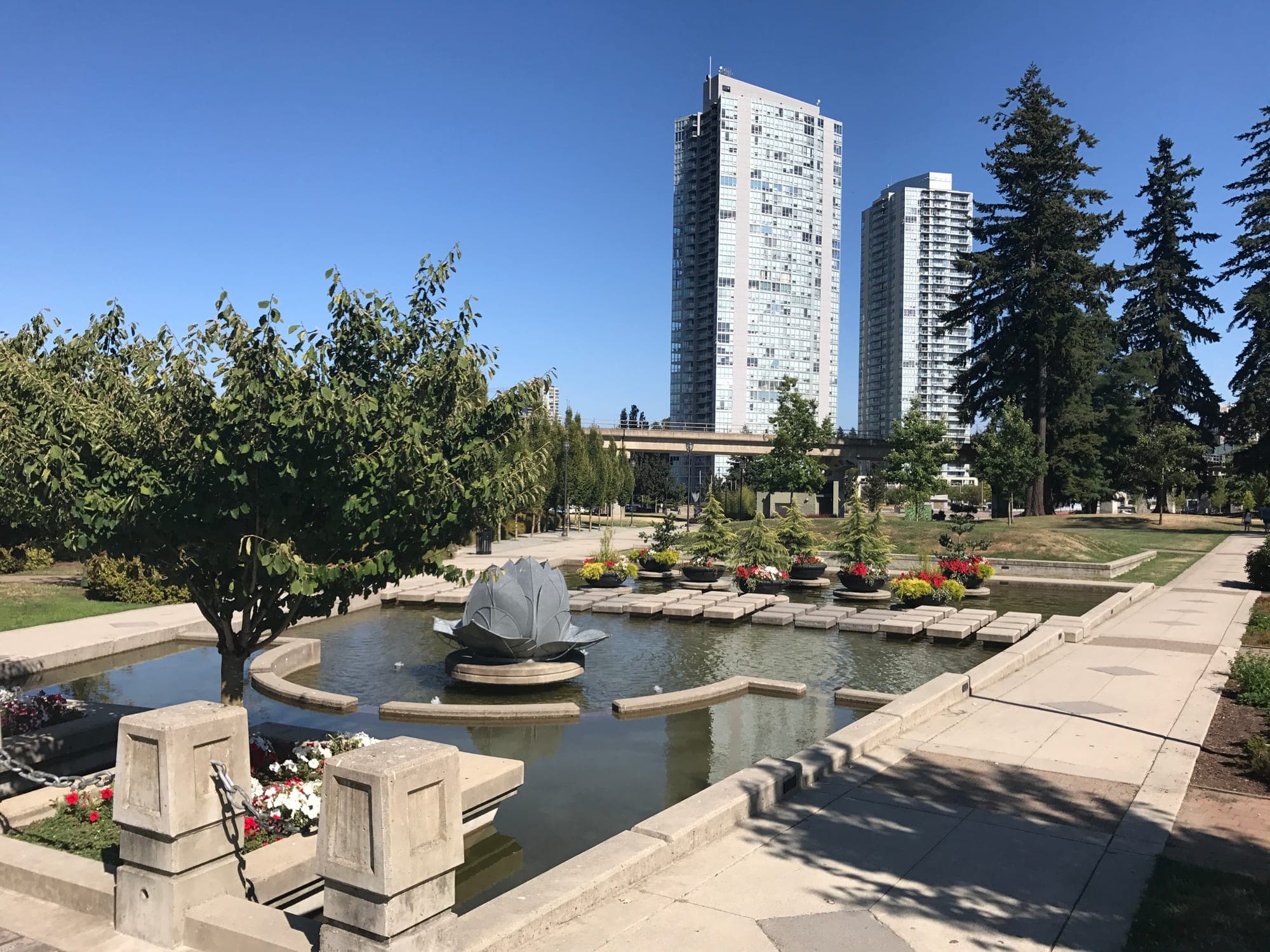 Holland Park in downtown Surrey with open lawns, mature trees, and the reflecting pool along Old Yale Road.
